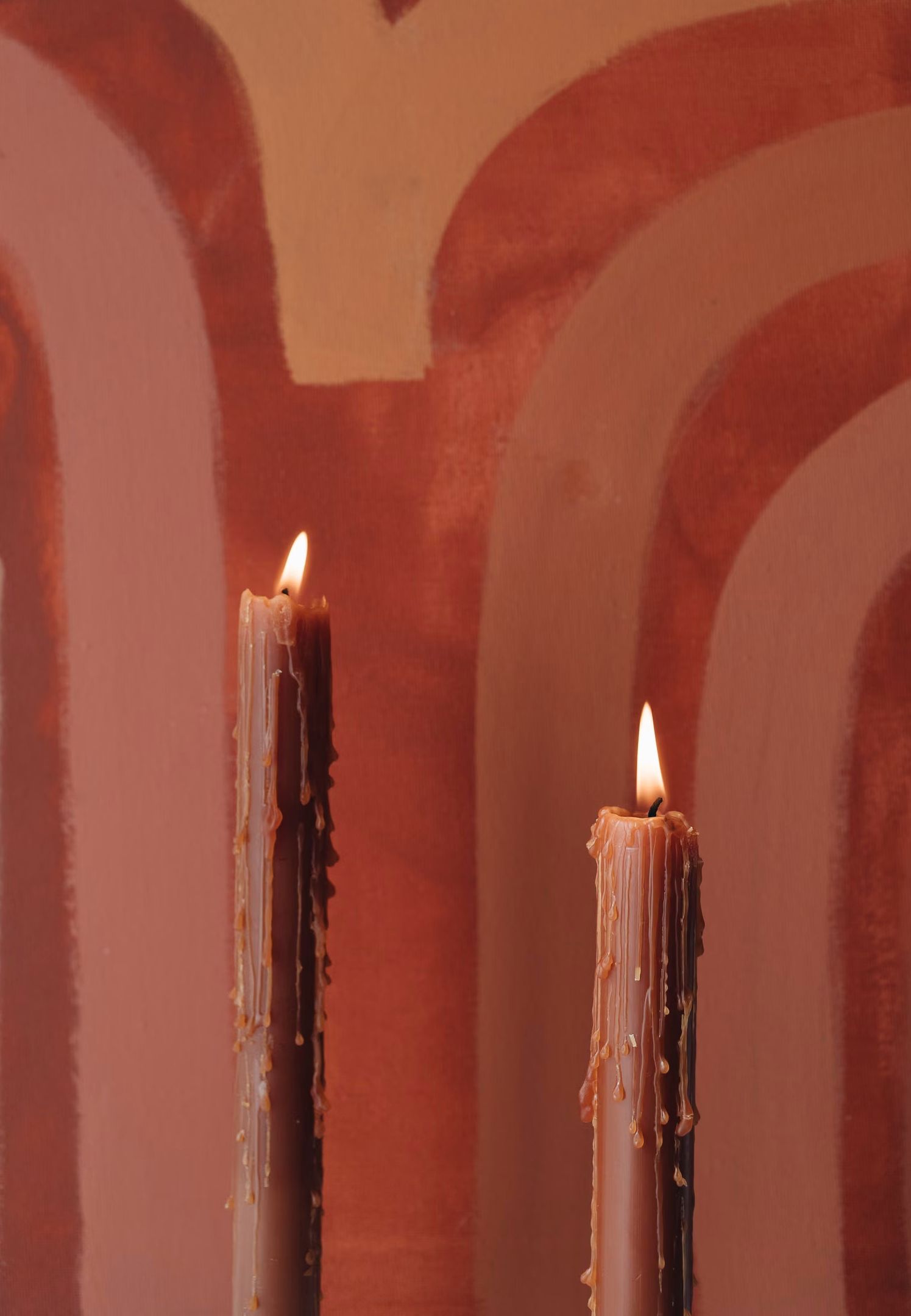 Deux bougies allumées à la cire orange fondue, devant une peinture abstraite aux tons rouges.